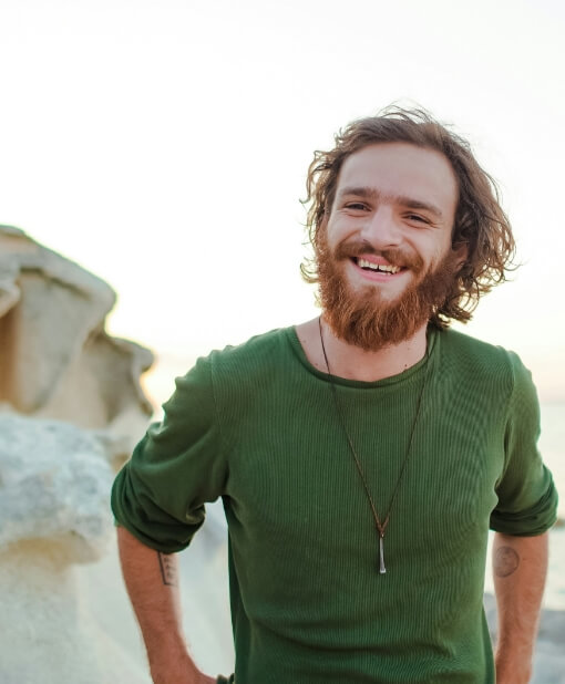 Cheerful man with a long beard and wavy hair smiling in an outdoor setting, exuding a sense of joy and relaxation.